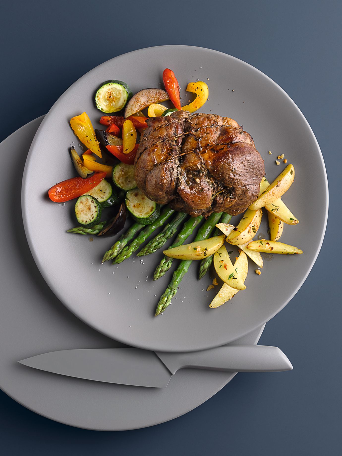 Leg of lamb on a bed of vegetables with potato wedges
