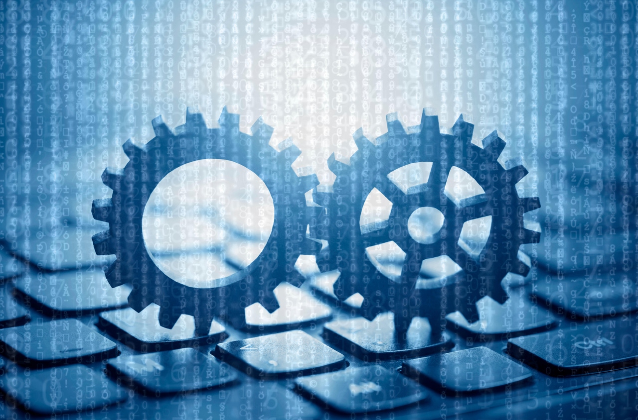 Two gears on computer keyboard with computer code in the background Two gears on computer keyboard with computer code in the background