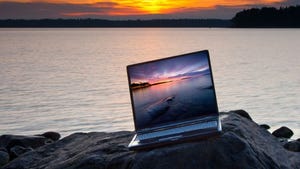 Laptop on rock in front of water displaying picture of sunset