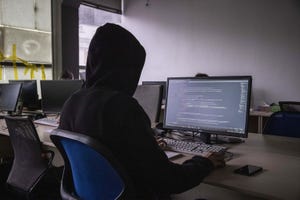hooded figure sits at a computer