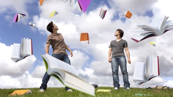 Two young men on grass with SQL Server books flying in the air