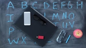 laptop, smartphone and apple in front of a chalkboard with the alphabet written on it