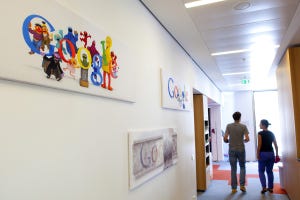 Two office workers walking down a hallway with Google logos hanging on the wall
