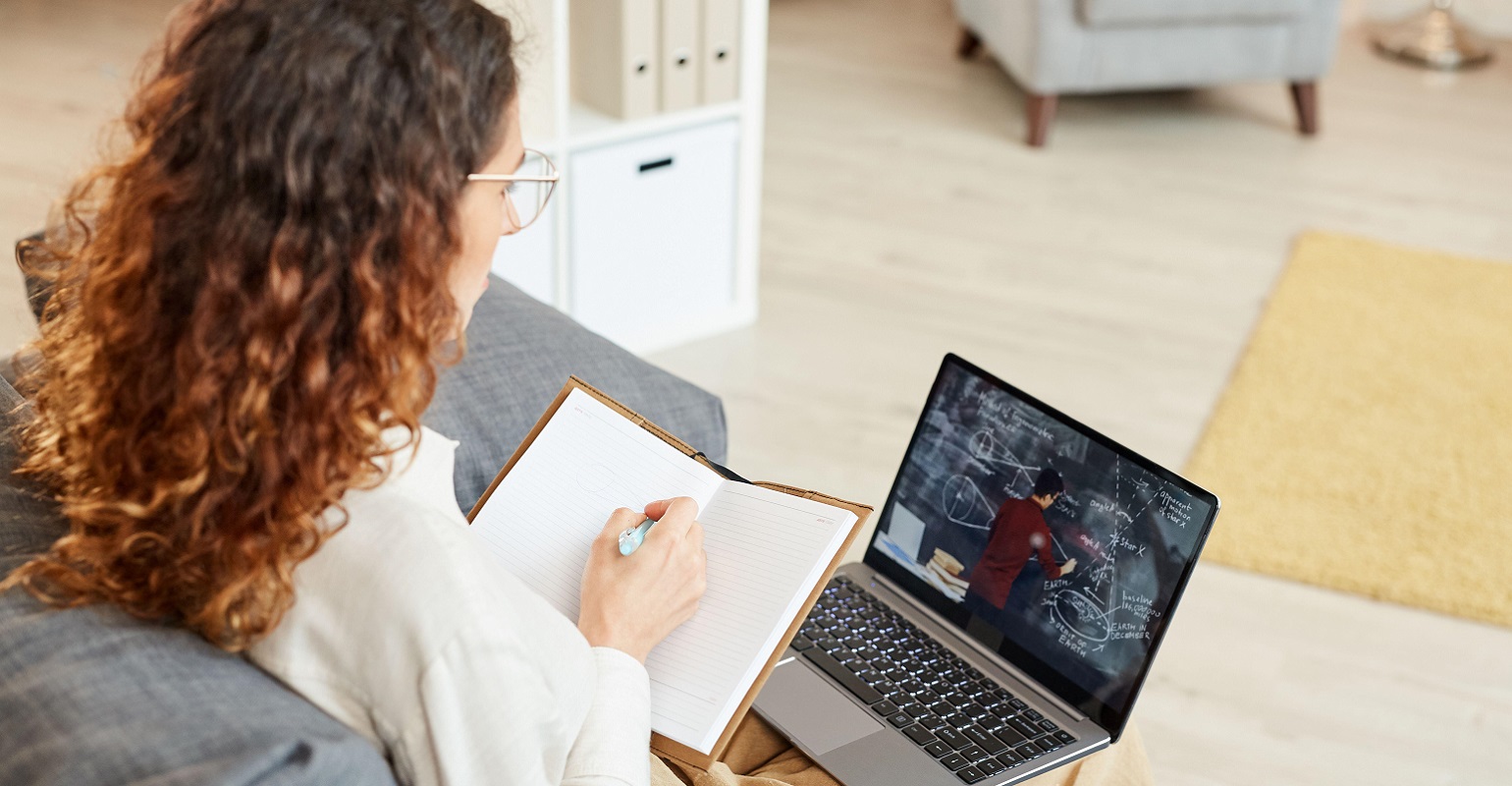 woman writing in a notebook while working on a laptop