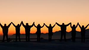 silhouettes of 8 people with arms raised at sunset