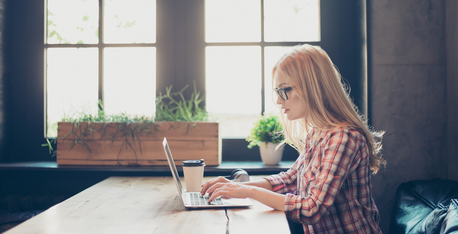 Side profile photo of woman wearing checkered shirt and glasses, typing on her laptop