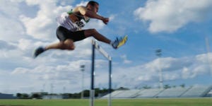 Man on track in running gear jumping over hurdle