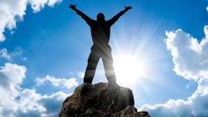 person on top of mountain with arm outstretched and sun silhouetting
