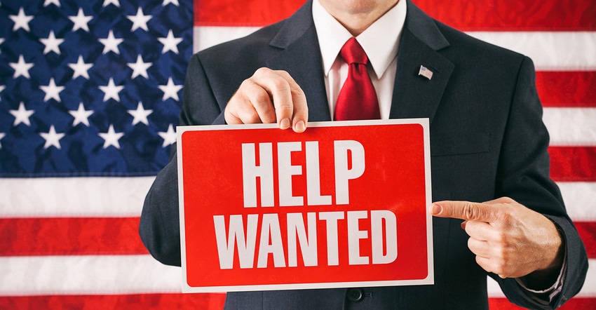 man holding help wanted sign in front of US flag
