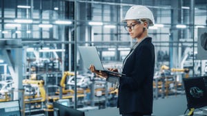 engineer wearing hard hat working on laptop in front of advanced manufacturing plant