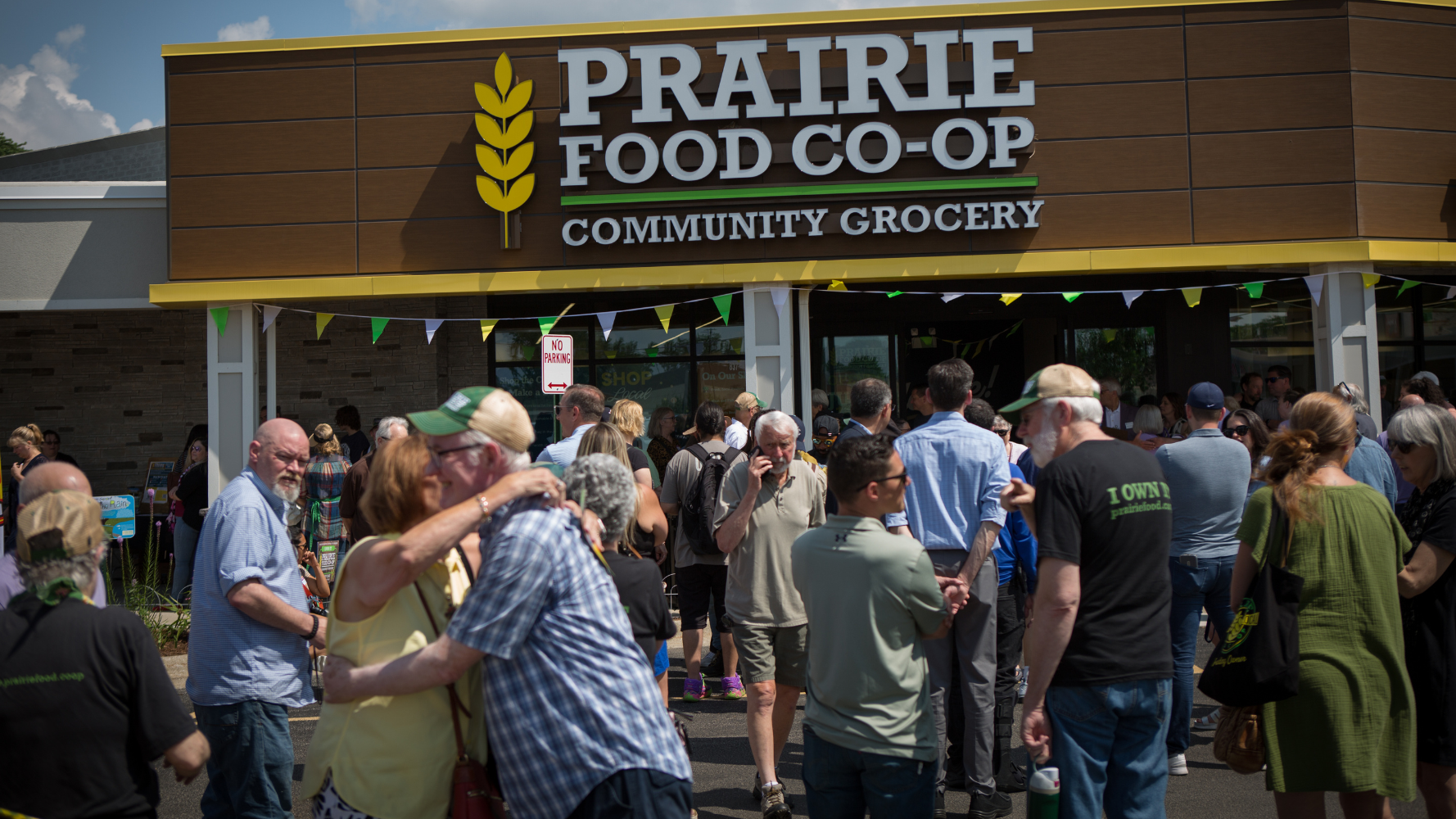 A crowd of people celebrating in front of the Prairie Food Co-op Community Grocery storefront.