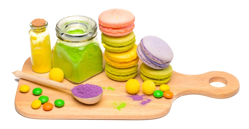 French macarons in different colors on a wooden serving board with powdered coloring