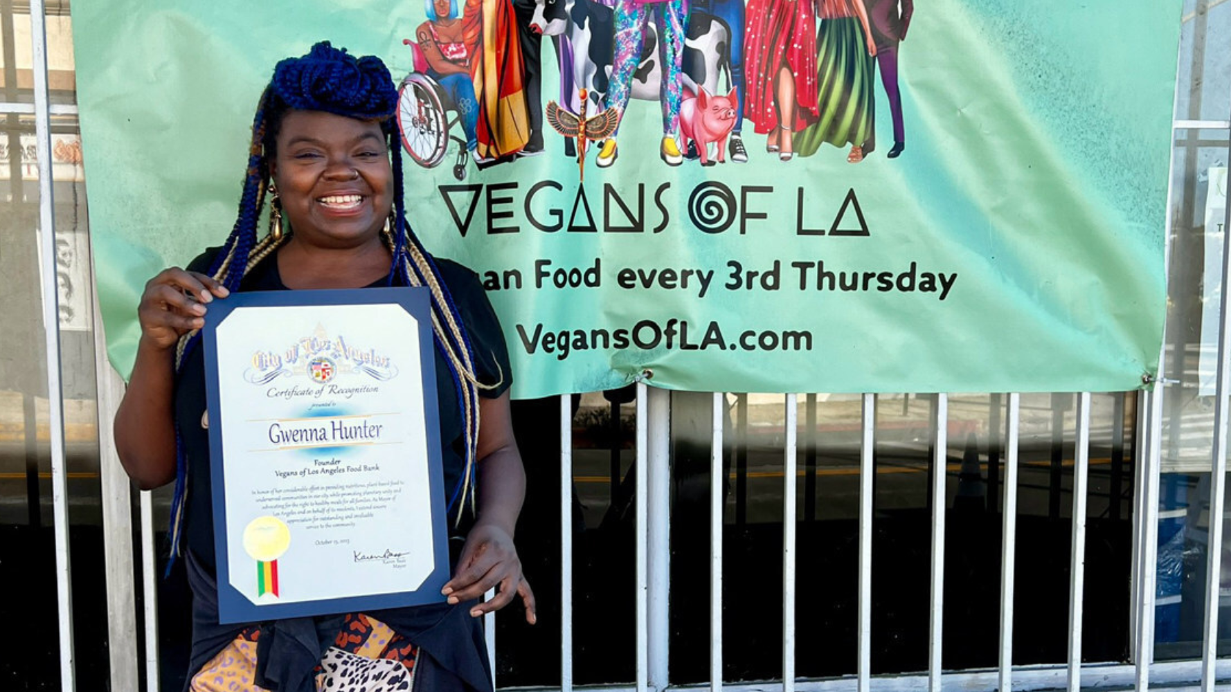 Gwenna Hunter, founder of Vegans of the Food Bank, poses in front of a banner while she has a recognition certificate in 2024. Gwenna Hunter, founder of Vegans of the Food Bank, poses in front of a banner while she has a recognition certificate in 2024.