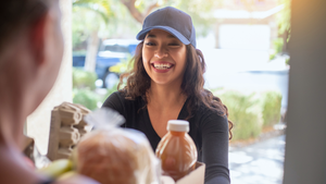 A smiling Black woman smiles at a white man who opened the door to accept his grocery delivery.  A smiling Black woman smiles at a white man who opened the door to accept his grocery delivery.