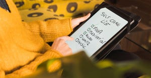 Woman in a yellow sweater examines a self-care checklist on an electronic tablet