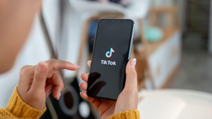 A woman holds a smartphone in her right hand as the TikTok app loads. Her left hand appears to be read to tap the screen when she sees what she wants. A woman holds a smartphone in her right hand as the TikTok app loads. Her left hand appears to be read to tap the screen when she sees what she wants.