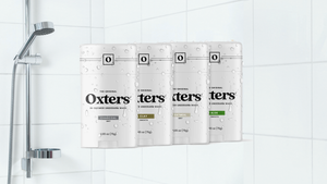 Four varieties of Oxters underarm wash are displayed in front of a shower with a handheld nozzle and tiles.  Four varieties of Oxters underarm wash are displayed in front of a shower with a handheld nozzle and tiles.