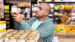 A man looks at a jar of spread while shopping in a retail grocery.  A man looks at a jar of spread while shopping in a retail grocery.