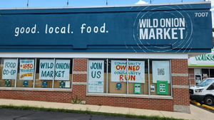 Wild Onion Market's windows are emblazoned with signs inviting nearby residents to become owners. One handwritten sign updates the number of owners. Wild Onion Market's windows are emblazoned with signs inviting nearby residents to become owners. One handwritten sign updates the number of owners.