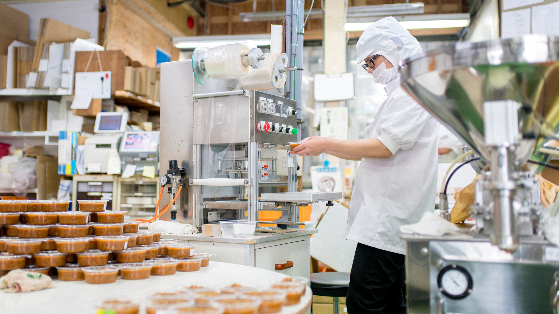 By hand, a food-processing employee fills individual plastic containers with salsa or dip. 