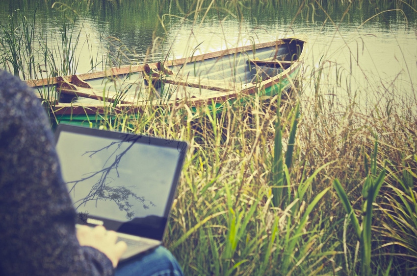Person working on laptop near pond with canoe