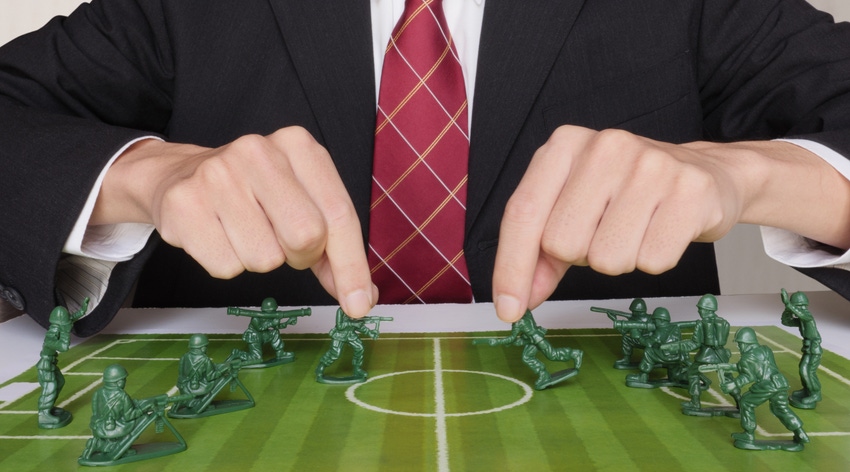 Businessman playing with toy soldiers on a soccer/football pitch. Photo illustration of business conflict, proxy war