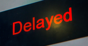 Close-up of the word "Delayed" in red letters on an airline schedule monitor at an airport.