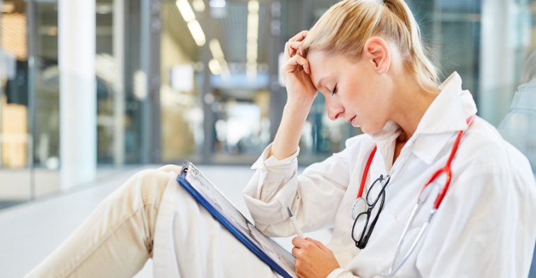 U.S. hospital staffing shortages is represented by this image of an exhausted female doctor or nurse sitting in a hospital
