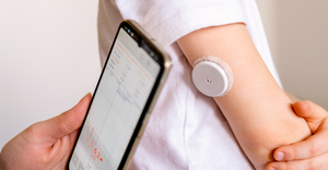 diabetes tech - child wearing a continuous glucose monitoring (CGM) sensor on their arm, a parent's hand holding a mobile
