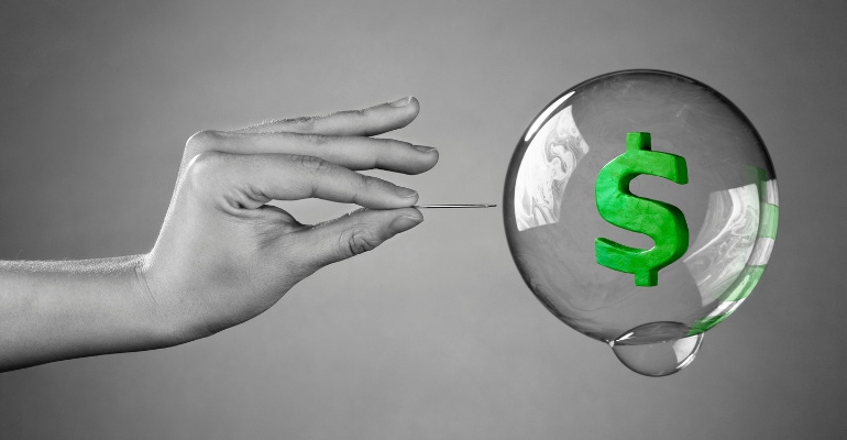 hand holding a needle about to pop a "money bubble" - financial market bubble bursting