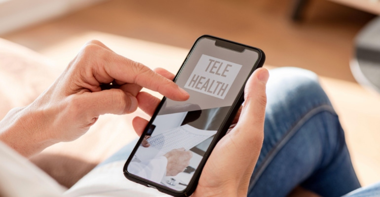 person holding a smartphone with the text "Telehealth" on the screen