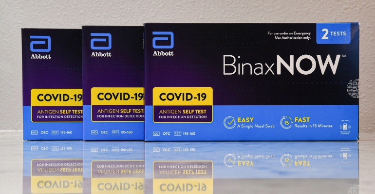 Photo illustration featuring three boxes of Abbott's BinaxNOW rapid COVID-19 test. The company is still seeing strong COVID