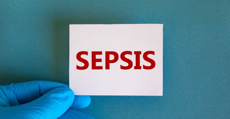Sepsis written on a card, held by a person wearing a medical glove.png