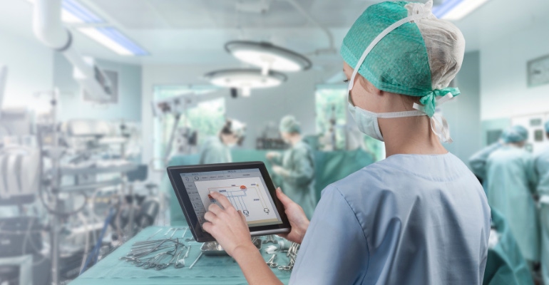 operating room nurse uses a digital tablet to operate medical devices in the OR; medical device cybersecurity concept