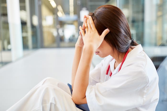 Tired nurse sits with head in hands during the global healthcare staff shortage.