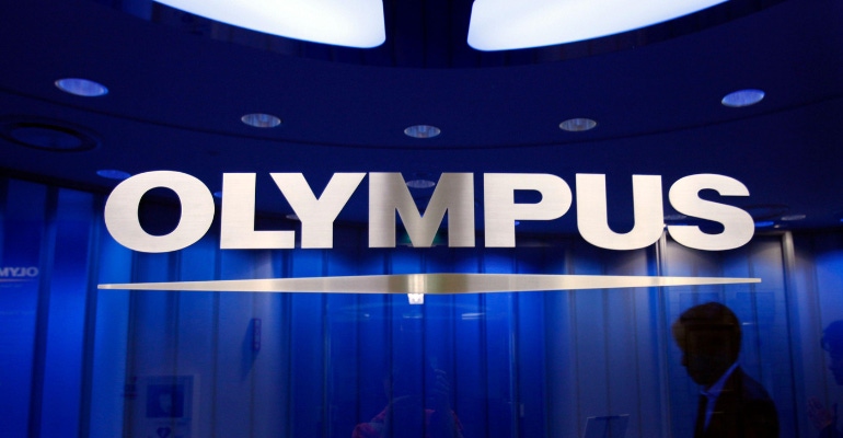 A man passes behind a logo of Japan's Olympus Corp at the company headquarters in Tokyo June 19, 2012.