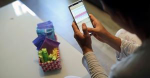 Woman using a period tracker app with a basket full of pads and tampons beside her.