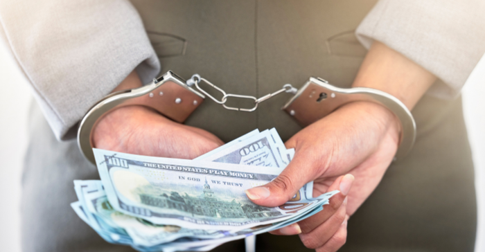 female executive in handcuffs holding a handful of cash in US currency