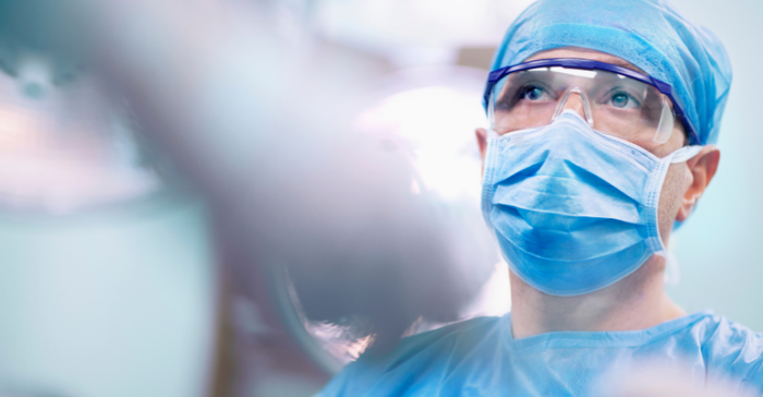 surgeon in operating room wearing PPE mask, cap, eye protection, and gown.png