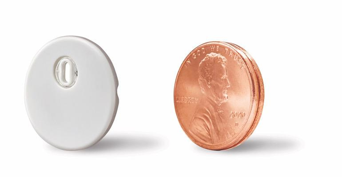 Libre 3 CGM sensor for diabetes management, shown beside two stacked U.S. pennies for size comparison
