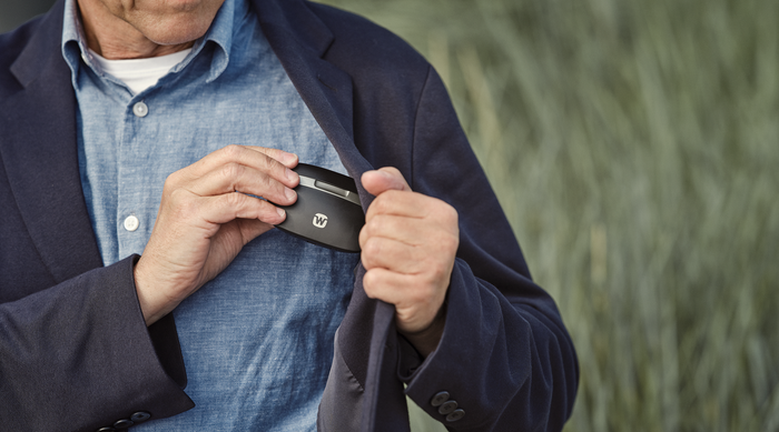 Widex SmartRIC hearing aid user slipping his portable hearing aid charging case into an inside jacket pocket