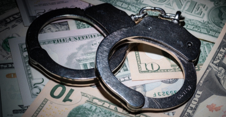 photo of a pair of metal handcuffs on top of a pile of U.S. currency