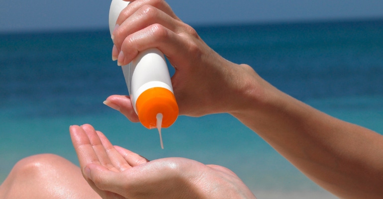 Woman at the beach applying sunscreen with closeup on the sunscreen bottle, no label.png
