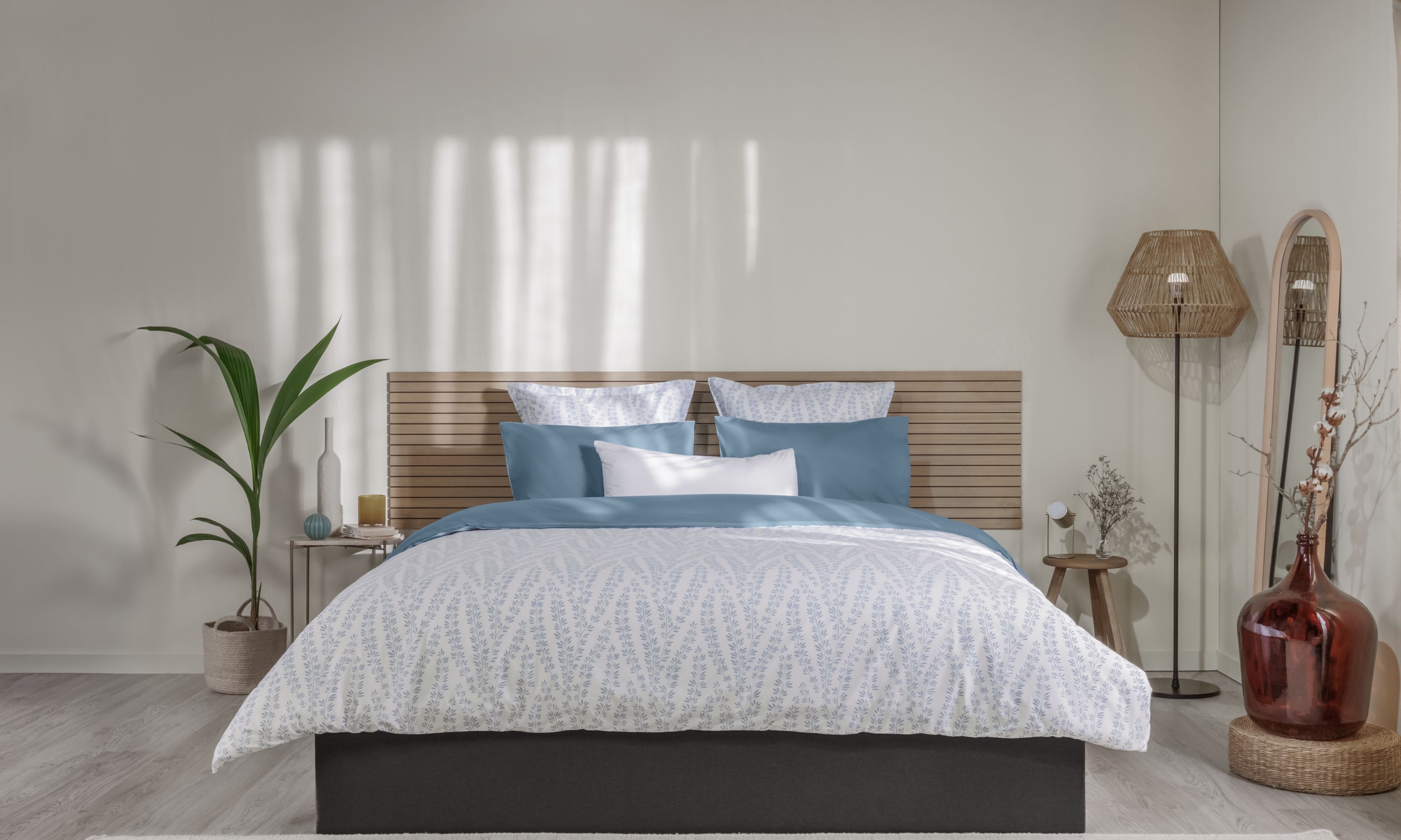 Letto ordinato con biancheria con motivo floreale bianco e azzurro, testiera in legno e decorazioni su entrambi i lati.