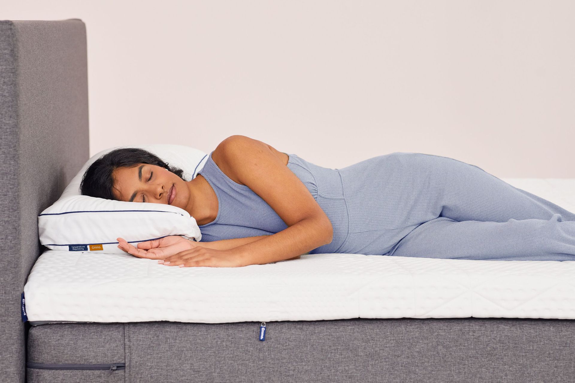 Femme allongée sur le côté sur un lit gris avec un matelas nu et un oreiller portant des logos Emma.