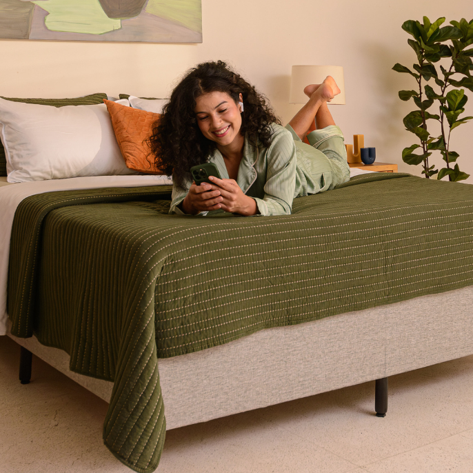 Pessoa deitada em cima de uma cama com o celular nas mãos