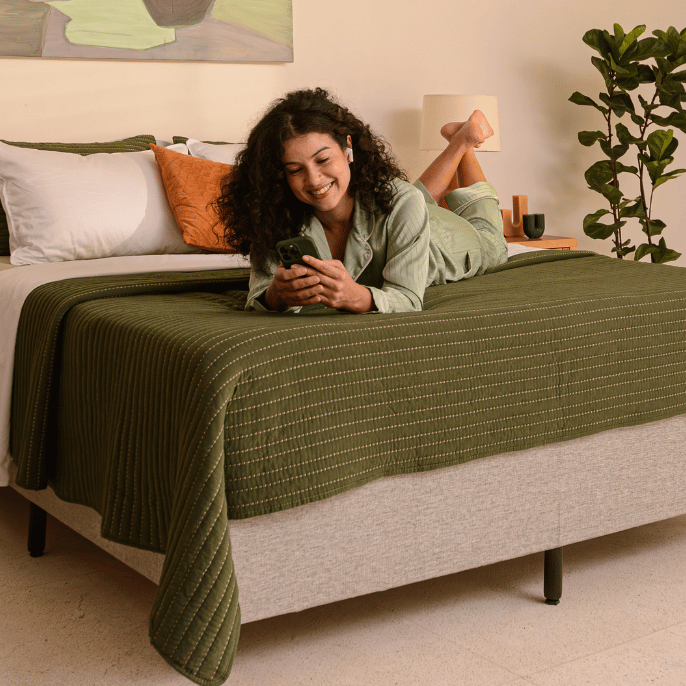 Pessoa deitada em cima de uma cama com o celular nas mãos