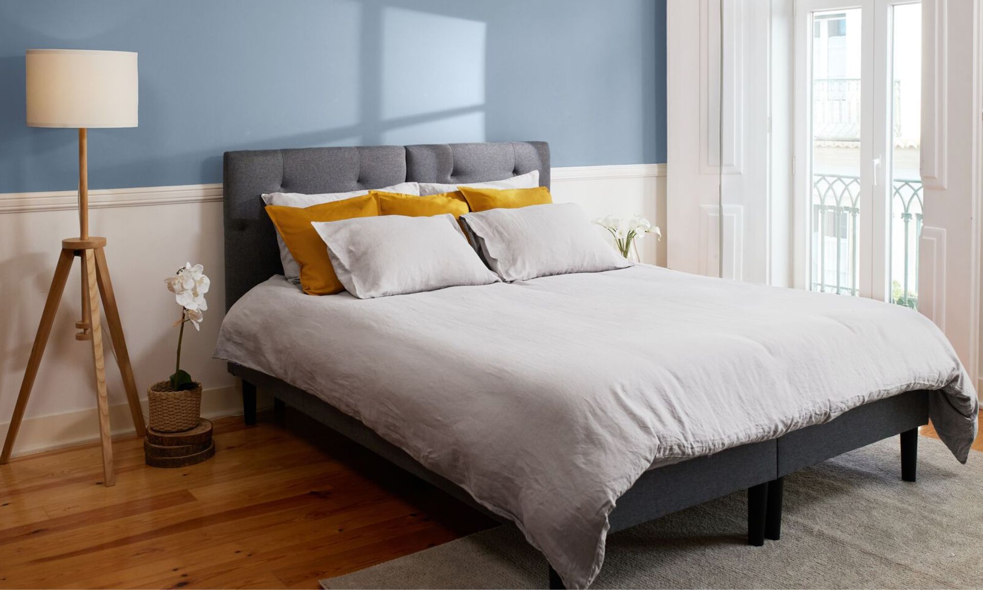 Camera da letto ordinata con parete azzurra, letto con testiera grigia e decorazioni naturali.