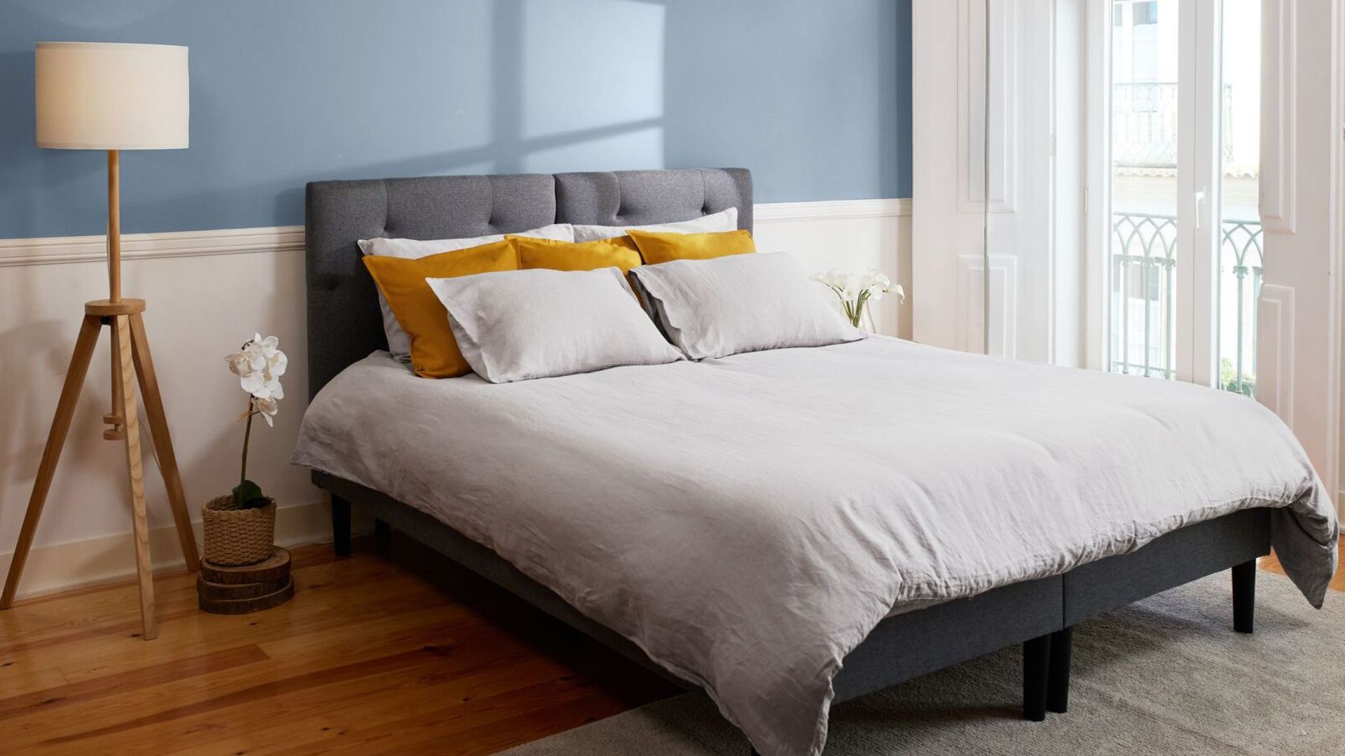 Camera da letto ordinata con parete azzurra, letto con testiera grigia e decorazioni naturali.