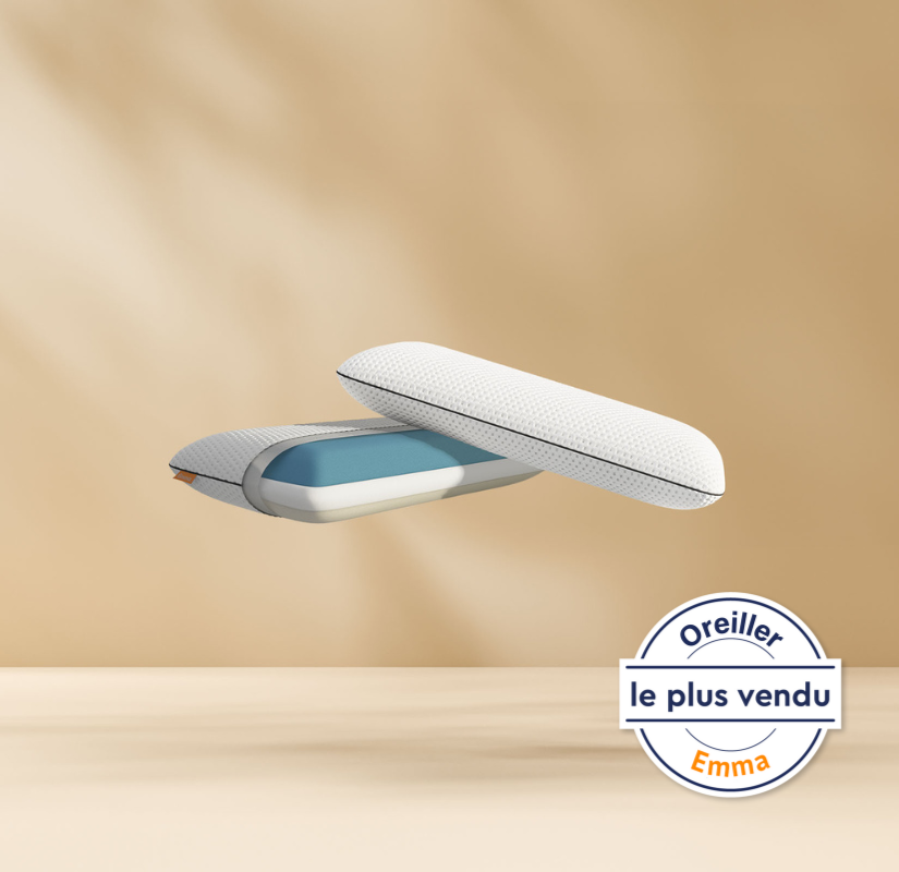 Deux coussins modernes avec une housse texturée blanche et une couche intérieure bleue flottent sur un fond beige. Un badge circulaire en français en bas à droite indique Oreiller le plus vendu Emma.